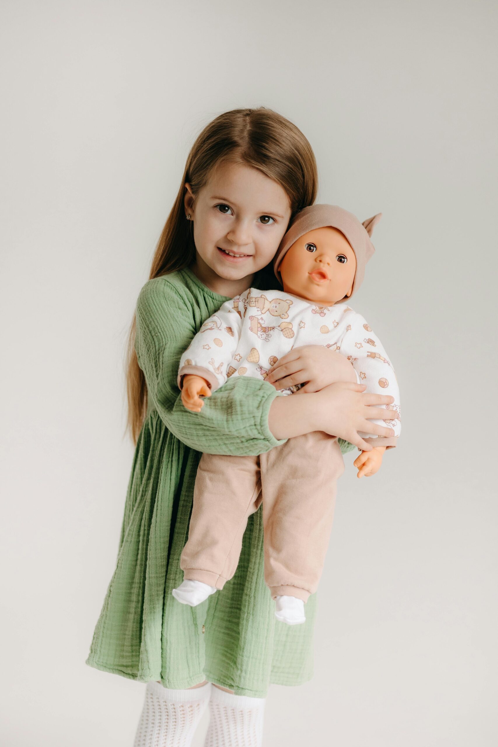 Adorable young girl in green dress holding a doll. Perfect for childhood and toy themes.