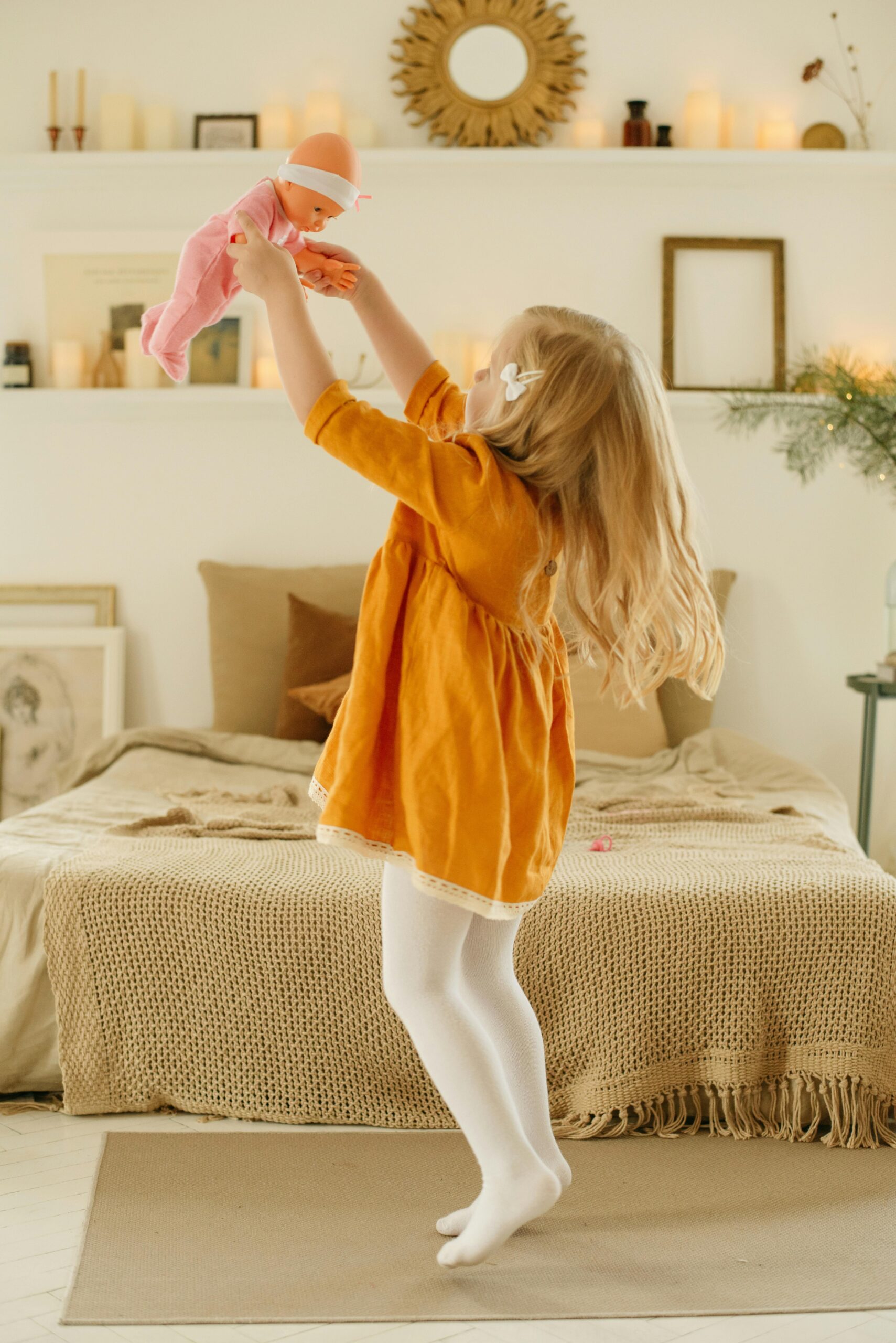 Cheerful child in orange dress playing with a doll in a cozy room.