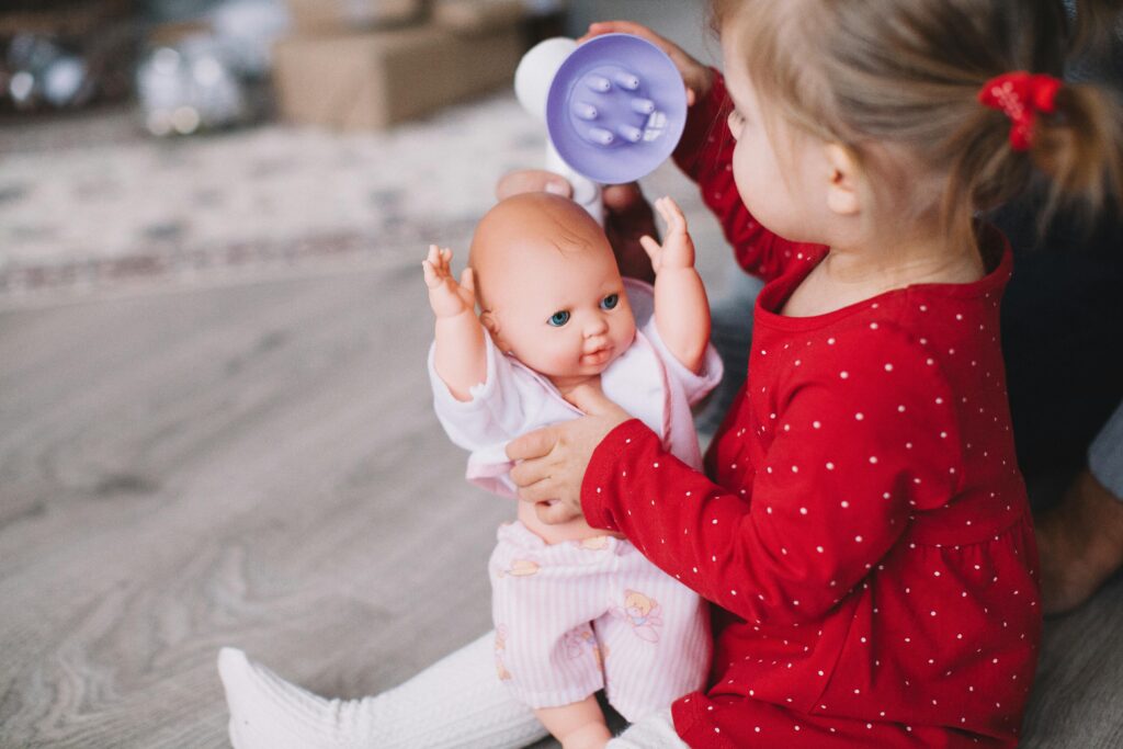 Child playing with a baby doll indoors, wearing a red dress.